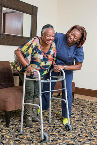 A home health care worker is helping a senior woman with a walker.